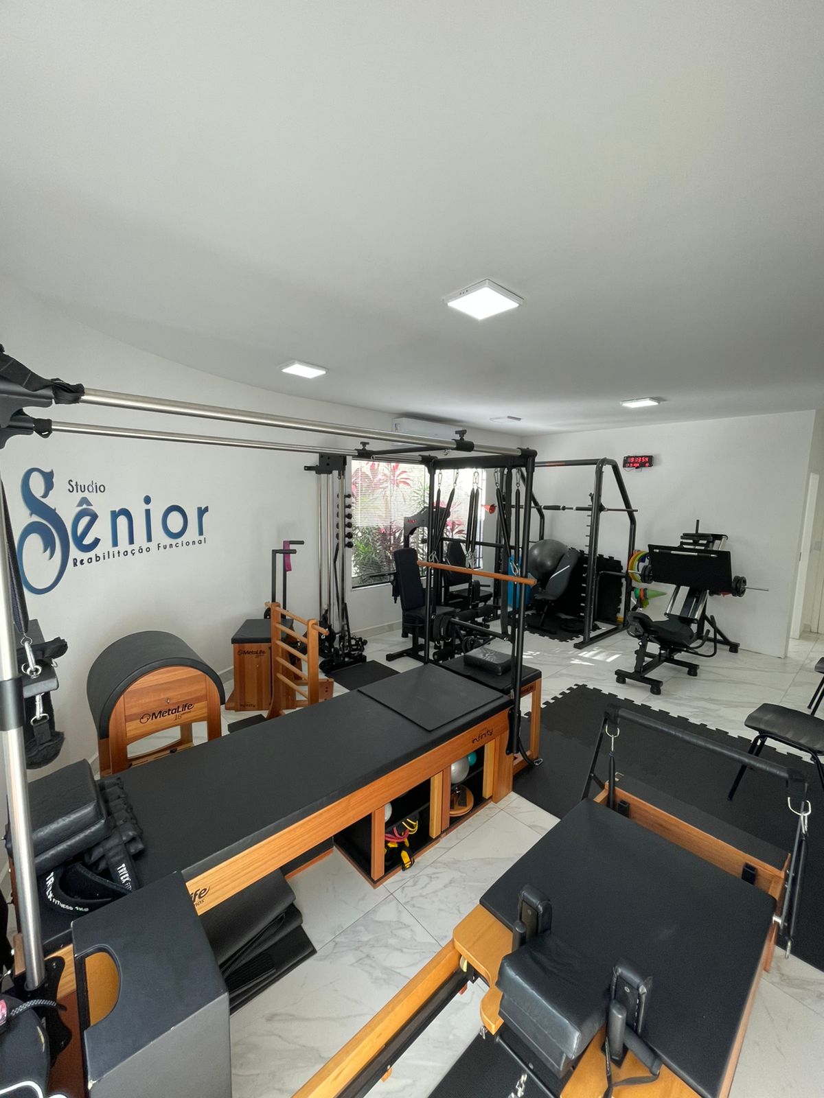 Visão geral do Studio Sênior com aparelhos de pilates, reformers e parede com a logo da clínica.