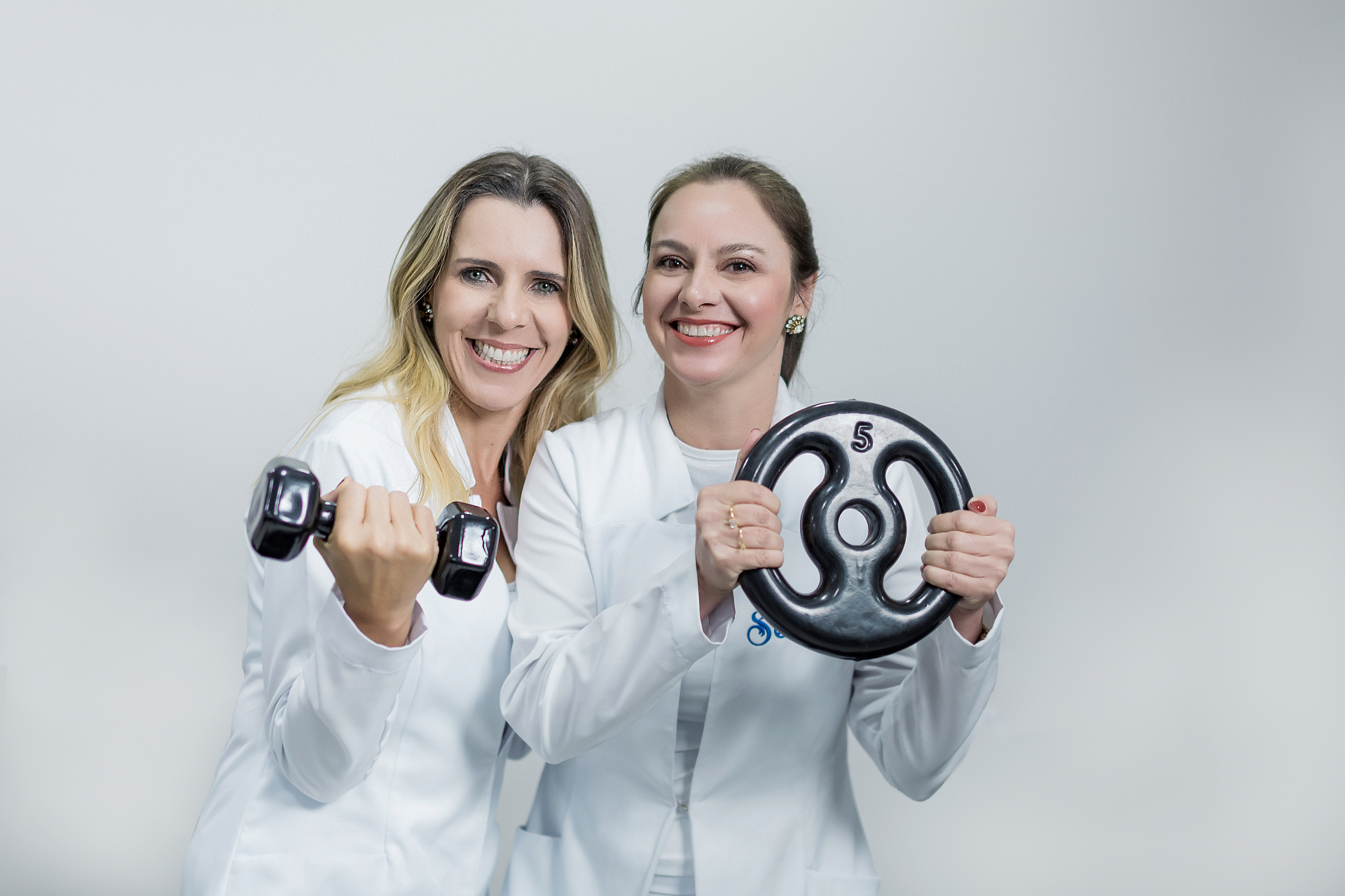 As duas profissionais do Studio Sênior segurando pesos durante ensaio fotográfico.